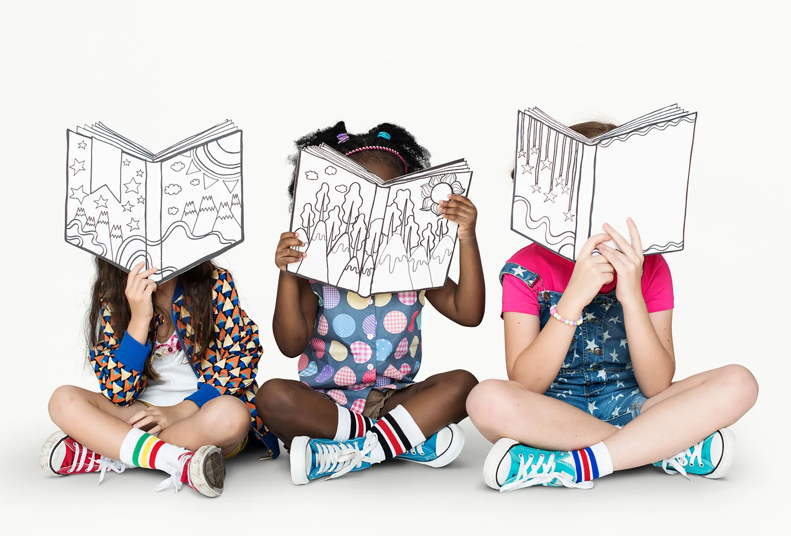 Drei Kinder sitzen auf dem Boden und halten Bücher hoch, die wie Zeichnungen aussehen